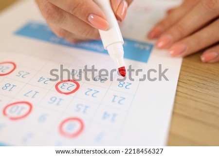 Close-up of female hand marking dates in calendar with red marker. Woman marked with bright felt pen important days. Planning and schedule concept Royalty-Free Stock Photo #2218456327