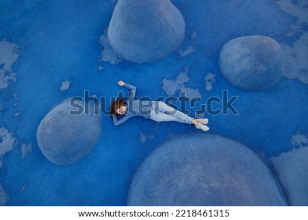 woman in blue jeans and a shirt is lying on a blue background on a sports field or in a park. a combination of colors, the blue color in life. a stylish woman is having fun and having fun. bright