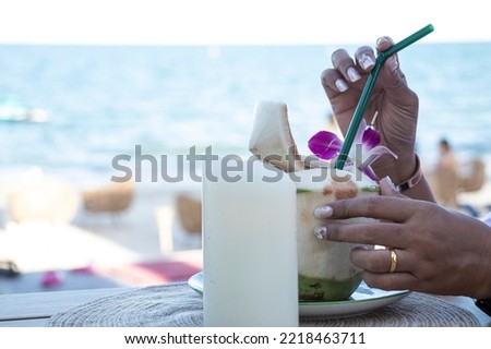 Woman's hand holding the young coconut fruit juice with  beach background. Relaxing moment. 