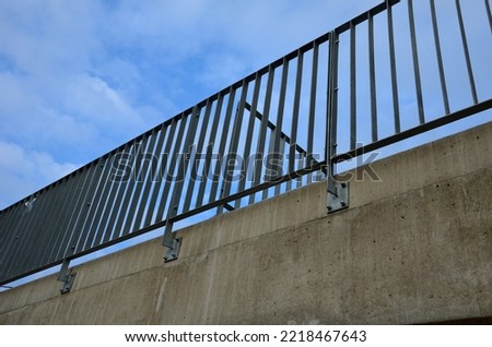 a bridge railing with vertical fence posts anchored into the ground with four concrete screws. the railing is fixed from the side of the bridge into the concrete.