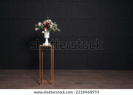 golden iron rack with white flowerpot with artificial flowers on a black background. white pot with flowers on the background of black walls in a photo studio. gothic style wedding photo zone