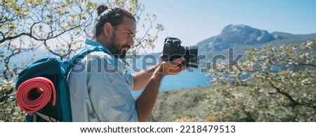 A man - a tourist with a backpack and a camera filming a landscape in the mountains. Young guy with camping equipment and a camera takes a photo or video near high rocks and blue sky