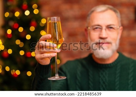 an elderly man in a green knitted sweater raising a toast with champagne near the Christmas tree