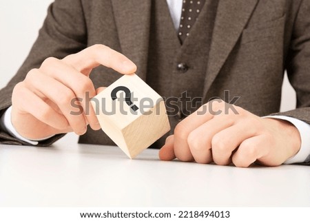 a business man's hand holds a wooden cube block with question marks on the corner
