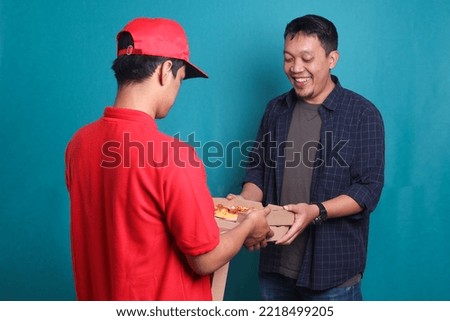 Man receiving boxes with pizza from courier male. Back view of delivery man delivering boxes with food to male client isolated on blue background.