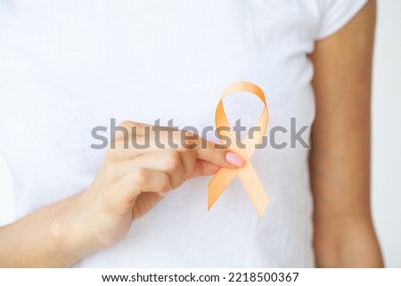 Woman in white t-shirt holding and showing orange awareness ribbon in her hands
