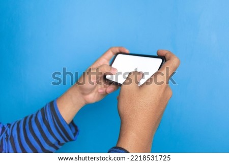 young adult man holding phone horizontal with white screen phone. illustrating a man playing game with his smartphone. isolated with blue background