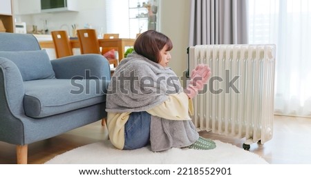 side view of asian woman covering blanket wearing gloves and wool hosiery feel cold using radiator heater to warm up sitting on floor at home in living room during winter Royalty-Free Stock Photo #2218552901