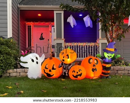 Illuminated night Halloween house outdoor decorations with inflatable figures of pumpkins, cat and ghost near house