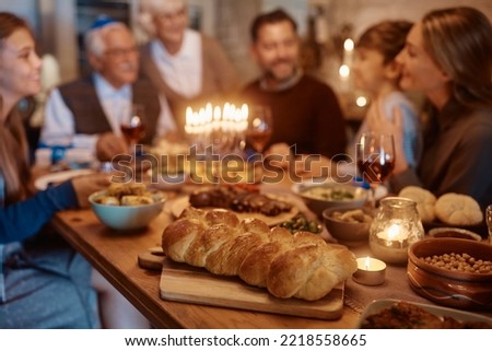 Challah bread on dining table with extended Jewish family in the background Royalty-Free Stock Photo #2218558665