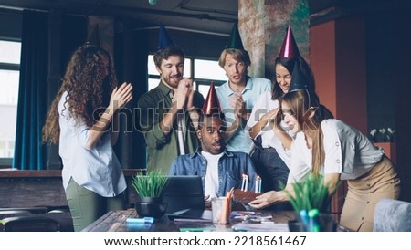 Group of young people is congratulating African American man on birthday in office bringing cake clapping hands and having fun.