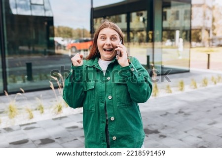 Beautiful woman in trendy wear spending time on street using smartphone. Happy Redhead girl talking on the mobile phone, warm sunny day. Urban lifestyle concept, technology banner