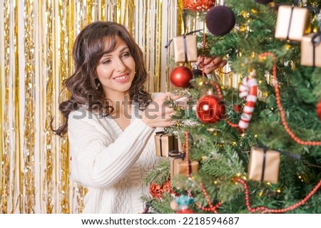 Pretty young woman in white sweater decorates Christmas tree, close-up. Concept of Christmas and New Year holidays