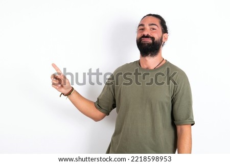 Smiling Caucasian man with beard wearing green t-shirt over white background indicating finger empty space showing best low prices