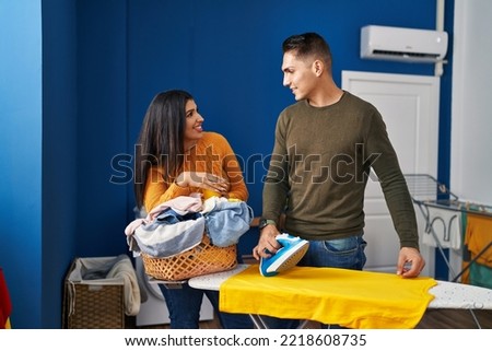 Man and woman couple smiling confident ironing clothes at laundry room