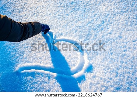 The heart is drawn in a snowy glade. Woman hand draws a heart in the snow.Background for the holiday of Valentine's Day. Cold heart, romance.Love symbol in the winter snow.Closeup,copy space. Royalty-Free Stock Photo #2218624767