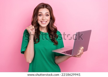 Photo of impressed excited pretty girl with wavy hairdo dressed green t-shirt clench fist hold notebook isolated on pink color background