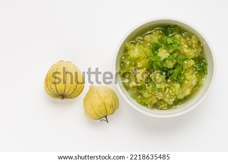 Physalis or tomatillo green dip in ceramic bowl with two whole fruits  isolated  top view. Vegetable salsa verde sauce