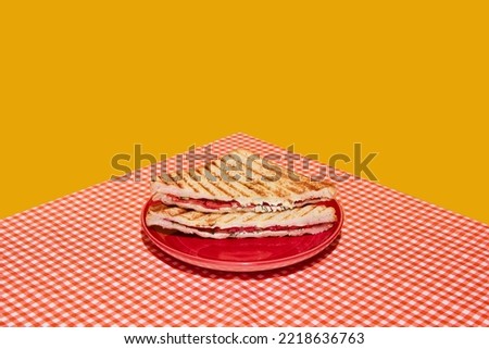 Light snack. Perfectionism and colorful minimalism. Meat sandwich, fried toast on plaid red and white tablecloth background. Food pop art photography. Vintage, retro 80s, 70s style. Royalty-Free Stock Photo #2218636763