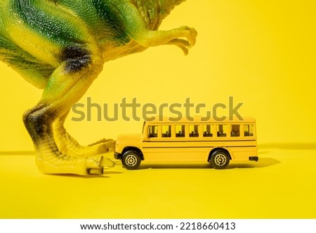 Giant toy tyrannosaurus rex with school bus on a yellow background.
