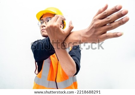 young asian male construction worker using yellow helmet and orange vest do stretching after hard working. stressed over work concept.  Royalty-Free Stock Photo #2218688291