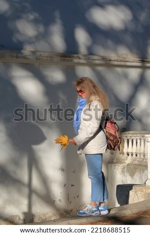 The photo was taken in the city of Odessa. In the picture, a young woman examines a bouquet of yellow autumn leaves.