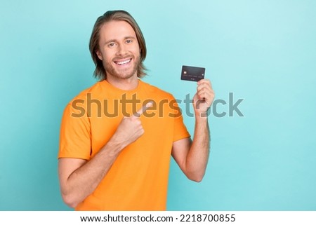 Photo of cheerful positive man wear orange t-shirt pointing finger credit card isolated turquoise color background