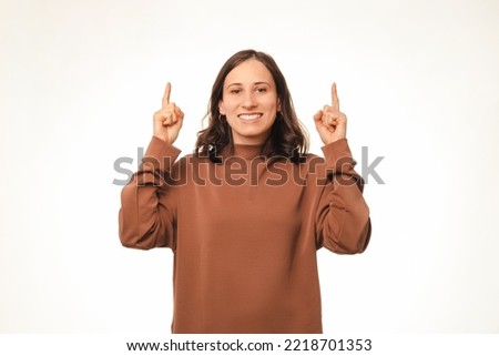 Portrait of young cheerful woman in hoodie pointing up with both hands over white background.