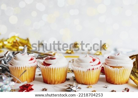 Four vanilla cupcakes with strawberry swirl icing lined up for a party among ribbon bows and confetti. Selective focus with blurred foreground and background. 
