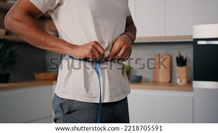 Unrecognizable sporty male sports man African guy measures waist with measuring tape check weight loss training workout sport dieting healthy nutrition control calories body muscle mass centimeters Royalty-Free Stock Photo #2218705591