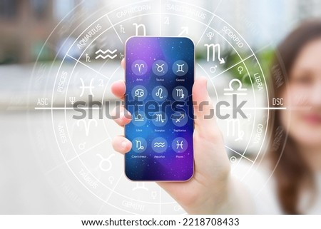A woman's hand holds a smartphone with an astrological application on the background of the street, astro forecast for all zodiac signs Royalty-Free Stock Photo #2218708433