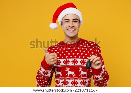 Merry young man wear red knitted christmas sweater Santa hat posing hold car key fob keyless system show thumb up isolated on plain yellow background. Happy New Year 2023 celebration holiday concept Royalty-Free Stock Photo #2218711167