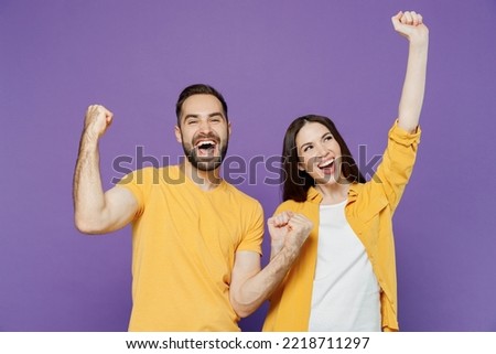 Young overjoyed excited couple two friends family man woman together in yellow casual clothes doing winner gesture celebrate clench fists say yes isolated on plain violet background studio portrait Royalty-Free Stock Photo #2218711297