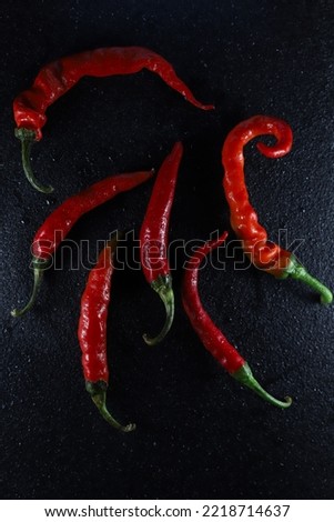 six saturated hot red chili peppers with green tails lie in a row on a black background with water drops. for restaurants menu shop signs labels flyers banners