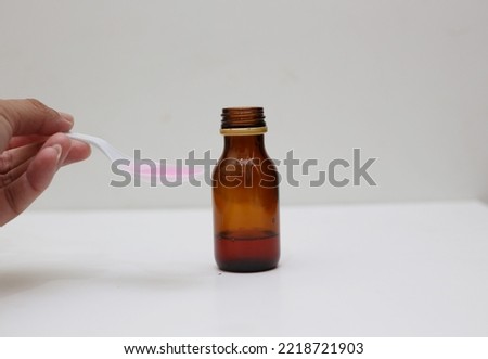 a bottle of liquid medicine or syrup and a plastic spoon filled with syrup. on a white background