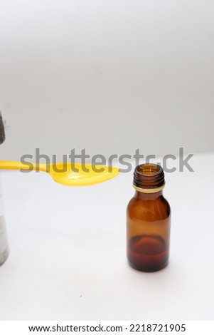 a bottle of liquid medicine or syrup and a plastic spoon filled with syrup. on a white background