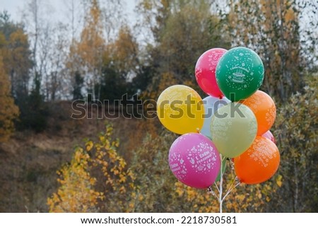 Ten colorful inflatable balloons in autumn forest. Balloons inflated with helium, birthday decoration outside. The inscription on ball in Russian means - happy birthday.