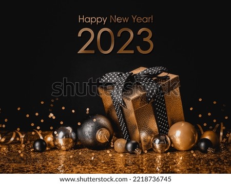 Happy New Year 2023! Congratulation Merry Christmas and Happy New Year. Golden box with a gift and Christmas balls on a black and gold background Royalty-Free Stock Photo #2218736745