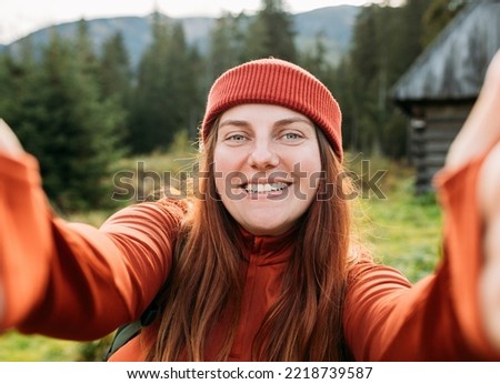 Woman in hat uses a telephone for take pictures, make selfies and video calls friends and family from home on mountains background. Travel and wanderlust concept. Amazing chill moment