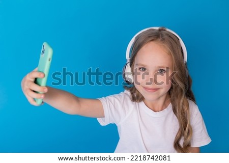 girl in a white T-shirt and jeans with headphones on her smartphone takes a selfie sitting on floor. High quality photo