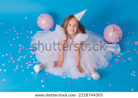 girl in a beautiful white fluffy dress and a festive hat is sitting on the floor on blue background. High quality photo