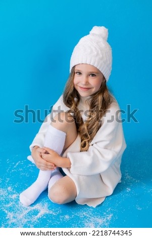 girl in a white sweater and hat blows artificial snow from the palm in the studio on blue background. High quality photo