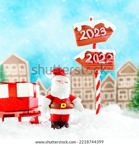 Santa Claus with sleigh and gifts in a toy town. Wooden direction signs 2023 and 2022. Waiting for the New Year 2023, Christmas card.