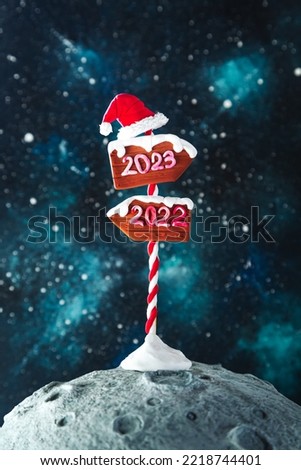 Wooden 2023 and 2022 direction signs and Santa's hat on the moon against the background of the night starry sky. Christmas background.