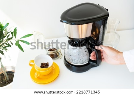 Beautiful morning, the girl is waiting for her coffee. Selective focus, noise. An automatic drip coffee maker stands with a yellow cup on a white table. Electric kitchen small household appliances Royalty-Free Stock Photo #2218771345