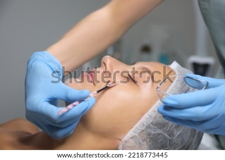 Cosmetologist applying chemical peel product on client's face in salon Royalty-Free Stock Photo #2218773445