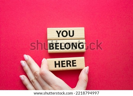 You belong here symbol. Wooden blocks with words You belong here. Beautiful red background. Businessman hand. Business and You belong here concept. Copy space.