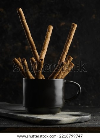 Cozy composition. On a dark background, a black cup with fragrant cinnamon sticks. Taste and smell of Christmas, New Year, family traditions, holidays. Spices, additives.