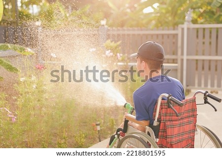 Behind of young man with disability water the plants in the garden,Hobby and Rehabilitation with natural therapy and Mental health, Exercise relaxation,planting day,Environmentally friendly concept.