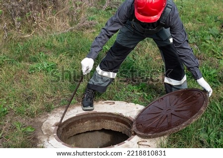 A male plumber opened the manhole of a water well for preventive inspection and repair. Royalty-Free Stock Photo #2218810831